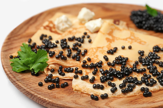 Thin pancakes with delicious black caviar on wooden plate
