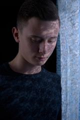 a handsome guy with a shade of curtains on his face stands in front of the window