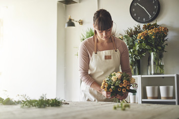 Young florist arranging a mixed flower bouquet in her shop - obrazy, fototapety, plakaty