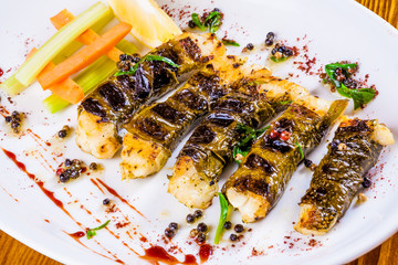 Pikeperch baked in grape leaves on white plate