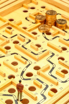 business man standing on wooden maze looking at a pile of coins faraway