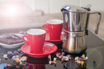 Caffettiera di acciaio inox e due tazze con il caffè caldo e cioccolato sul piano di cottura a induzione