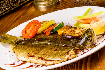 Whole trout with grilled vegetables on white plate