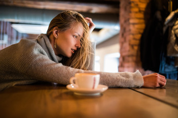 Attractive female student sits at cafe with cup of coffee, wants to have rest, being tired and exhausted. Dreamful woman in glasses sits at cafeteria