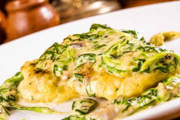 Pike-perch fillet baked with cheese, mushrooms and spinach on white plate