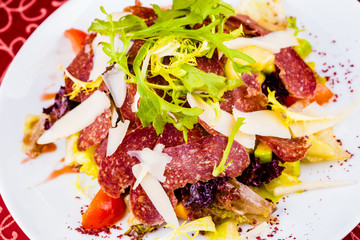 Salad with salami, vegetables and cheese on white plate. Close-up