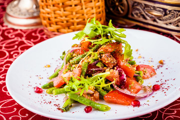 Salad with green beans, onion, tomatoes and walnut sauce on white plate. Georgian cuisine