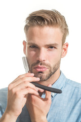 Barbershop concept. Attractive yound barber with beard and mustache while holding straight razor near his beard. Bearded handsome, sexy macho with straight razor in hand poses in studio. Closeup.