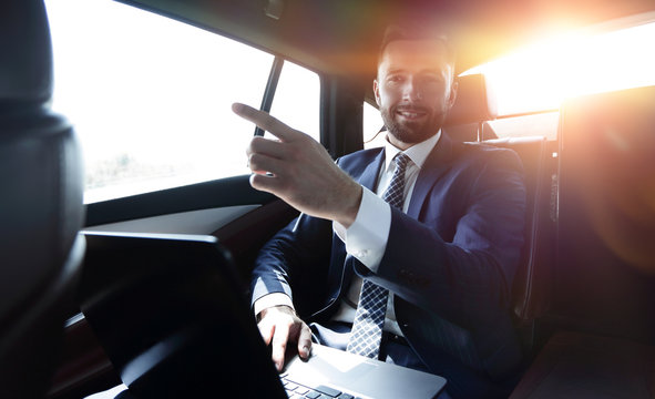 businessman sitting in the back seat in the car and pointing his finger forward