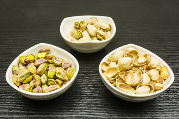 Shelling pistachio nuts. Whole, nutshell and peeled pistachios in bowls.
