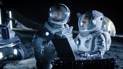 Two Astronauts Wearing Space Suits Work on a Laptop, Exploring Newly Discovered Planet, Send Communicating Signal to Earth. Space Travel, Interstellar Exploration and Colonization Concept.