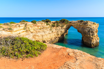 Green plants on cliff and view of rock arch on sea near Armacao de Pera town, Algarve, Portugal