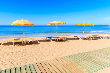 Wooden walkway and sun loungers with umbrellas on beautiful sandy Praia da Rocha beach in Portimao town, Algarve, Portugal