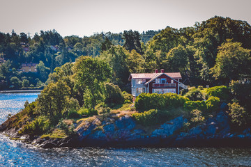 A view of the residential house, standing on the hill of a forest island with a stone shore on a sunny bright day, Sweden