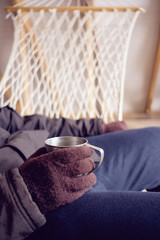 man holding mug of coffee or tea while sitting in hammock in winter hut