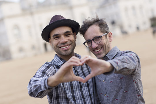 homosexual couple making a heart symbol with their hands.