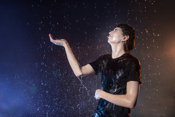 Fototapeta na wymiar Attractive young man in black wet clothes under the rain and splash of water, studio photo