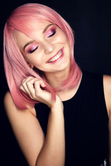 Model with pink make-up and pink hair is laughing. Portrait of a girl on a black background