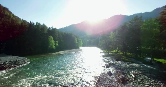 4k (UHD) aerial view. Low flight over fresh cold mountain river at sunny summer morning. Green trees and sun rays on horisont.