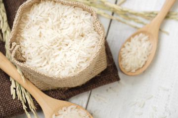 A wooden spoon filled with rice placed on wooden background.