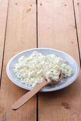 Cheese, fresh cottage cheese in a white plate, wooden spoon, curd on a wooden background, sour cream in a wooden spoon, dairy products on a natural background, retro style, minimalism