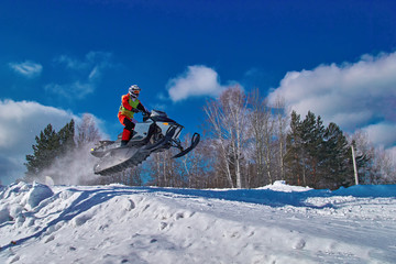 Sports race snowmobiles. Snowmobile in jump above track. Sportsman on snowmobile. Winter competition, sunny day. Copy space.