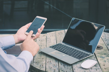 attractive hand of business man using smartphone and laptop working on wood table at outdoor.