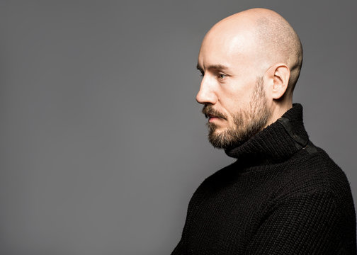 Fashion Portrait of a 40-year-old man standing over a light gray background in a black sweater. Close up. Classic style. Bald shaved head. Copy-space. Studio shot
