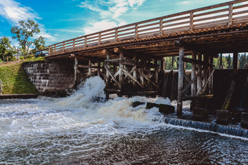 Wooden bridge over the river with a waterfall sunny clear day against a cloudy sky background