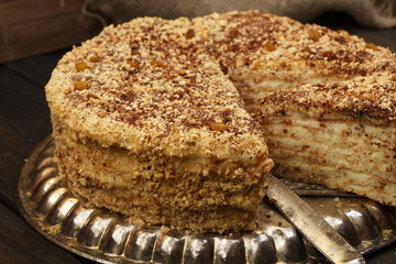 Napoleon's cake with custard is decorated with raisins and grated chocolate on a silver platter on a wooden table. Dessert Napoleon cake chopped. Napoleon cake tasty close-up.
