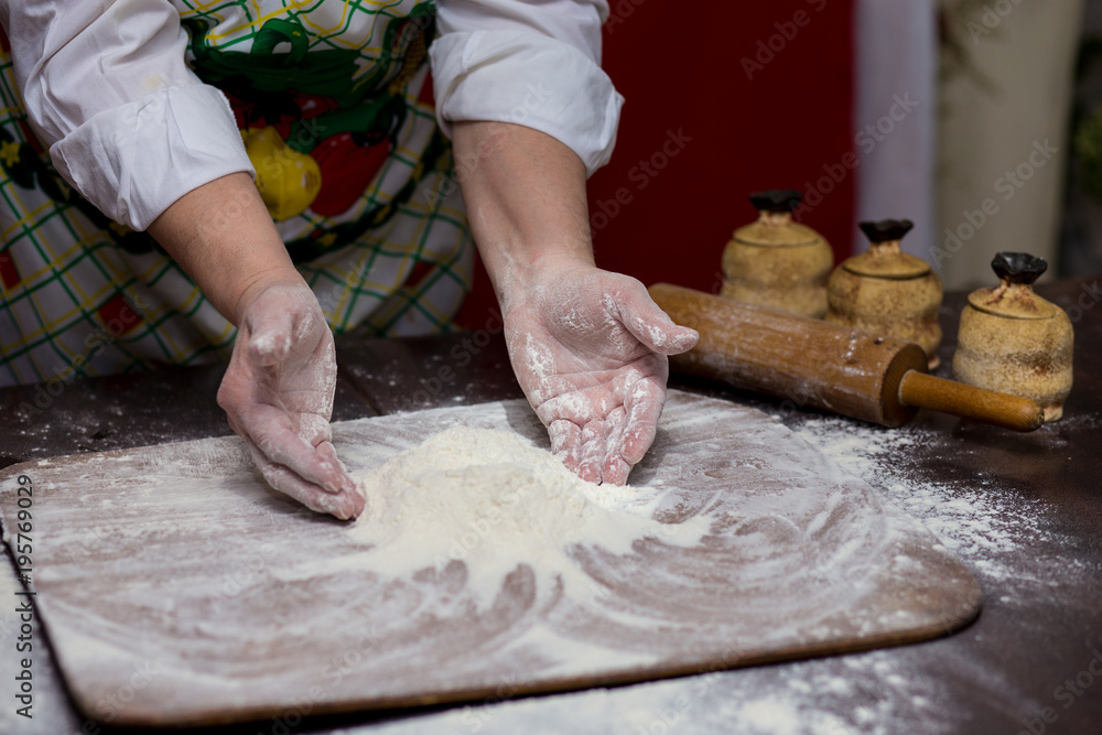 Wall mural a woman cook sprinkling flour over a cutting board. cooking. making bread on kitchen table. cooking 