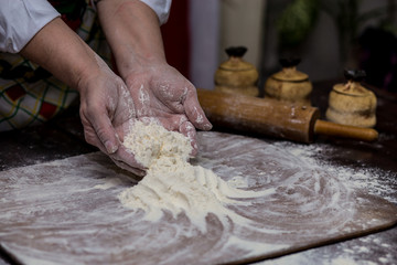 A woman cook sprinkling flour over a cutting board. Cooking. Making bread on kitchen table. Cooking Process Concept