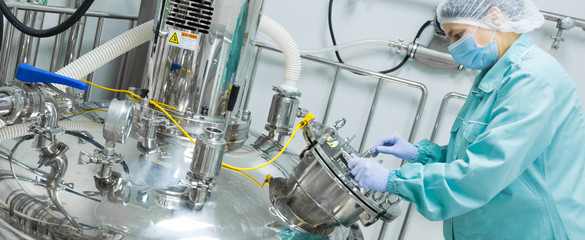 Pharmaceutical factory woman worker in protective clothing operating production line in sterile...