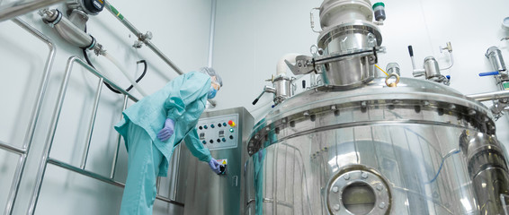 Pharmaceutical factory woman worker in protective clothing operating production line in sterile...