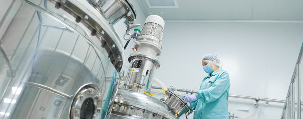 Pharmaceutical factory woman worker in protective clothing operating production line in sterile...