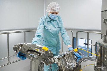 Pharmaceutical factory woman worker in protective clothing operating production line in sterile...