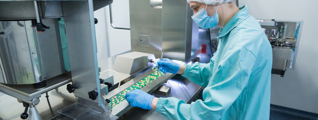 Pharmaceutical industry man worker in protective clothing operating production of tablets in...