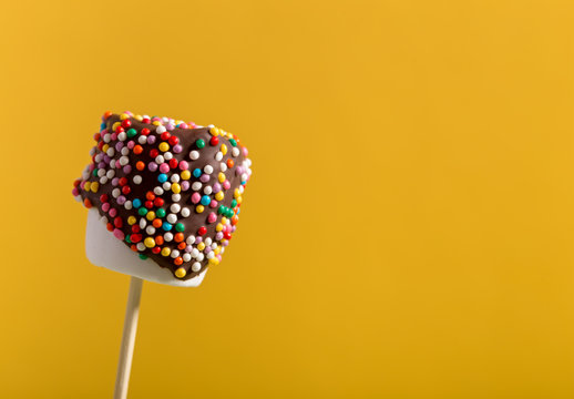 Homemade chocolate covered marshmallow on golden-yellow background with copy space