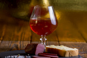 A glass of cognac stands on a wooden table with meat and lemons