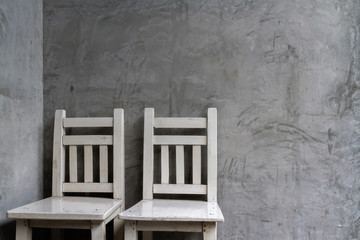 Fototapeta na wymiar Two old white wooden chairs in front of dirty and crack cement wall, Still life image and under roof lighting background