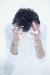 Vertical close up portrait of brunette male dressed in t-shirt starting cold winter morning with washing face with white snow to promote health, sitting on knees at ground. Wellness and beauty concept