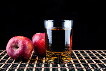 glass of juice and red apples on a black background