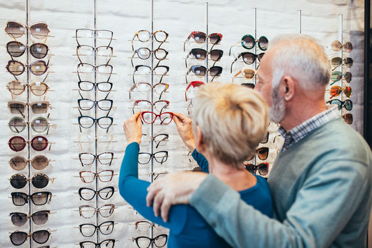 Happy senior couple choosing together eyeglasses frame in optical store. 