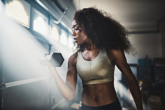 fit african american woman working out by lifting weights in home gym