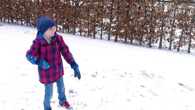 boy having fun in the snow throwing snowball in slow motion