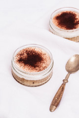 Italian Tiramisu dessert served in a glass cup made of coffee flavoured genoise sponge cake topped with mascarpone vanilla cream and dusted with cocoa on white with vintage spoon