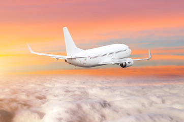 Obraz premium Passanger airplane above the clouds horizon sky with bright sunset colors.