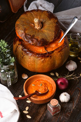 pumpkin cream soup poured into a baked pumpkin. still life in a rustic style. pumpkin seeds and spices next to the table.