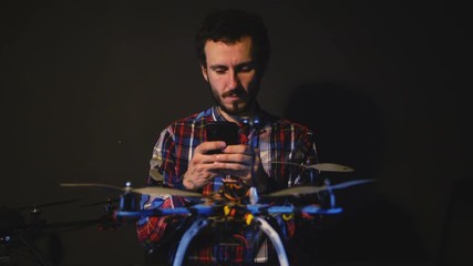 Young bearded Male Engineer work with drone in workshop. Computers and monitors background. - Powered by Adobe