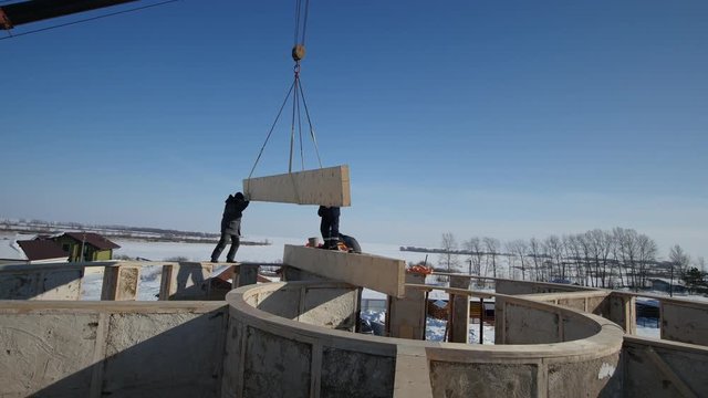 Working crane boom - constructions of private cottage with wooden straw block - winter construction site